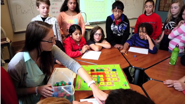 Teacher demonstrating to students around a table how to play a board game.